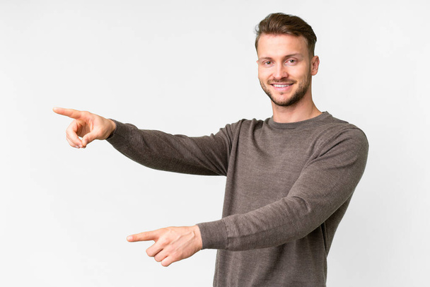 Junger gutaussehender kaukasischer Mann über isoliertem weißem Hintergrund, der mit dem Finger zur Seite zeigt und ein Produkt präsentiert - Foto, Bild