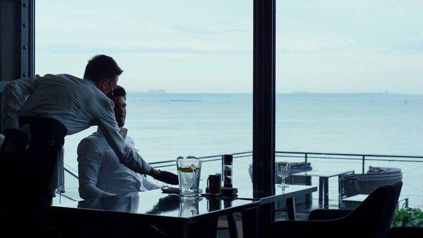 Relaxed man resting hotel cafe terrace at lunch time break. Elegant masked waiter serving meal to successful businessman customer. Joyful entrepreneur silhouette enjoying sea view in luxury restaurant - Photo, image