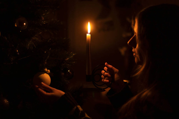 Ucrania, invierno de 2022. Una mujer decora un árbol de Navidad en la oscuridad con una vela. - Foto, imagen