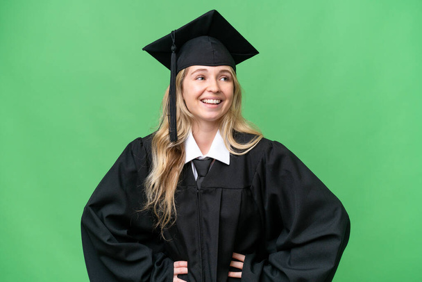 Joven universitaria inglesa graduada sobre fondo aislado posando con los brazos en la cadera y sonriendo - Foto, Imagen