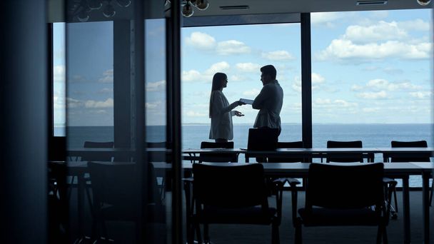 Silhouette colleagues talking ocean panorama window office. Unknown company managers team looking solution together at marine view. Nervous businessman leaving dark interior office workplace - Фото, изображение