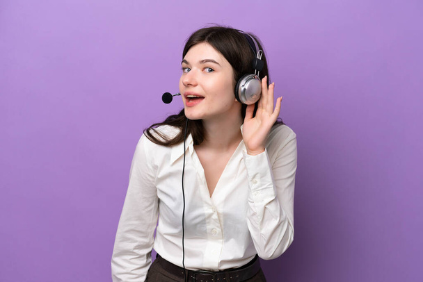 Telemarketer Russische vrouw werken met een headset geïsoleerd op paarse achtergrond luisteren naar iets door de hand op het oor - Foto, afbeelding