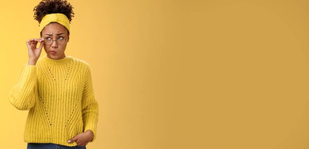 Inseguro pensativo vacilante lindo afroamericano millennial adolescente en gafas redondas suéter diadema resolver acertijo mente buscar dudoso toque gafas sonriendo, pensando fondo amarillo. - Foto, imagen