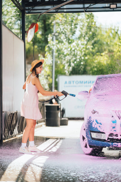 Brünette mit langen Haaren aus einem Hochdruckschlauch trägt in einer Waschanlage einen Reiniger auf das Auto auf - Foto, Bild