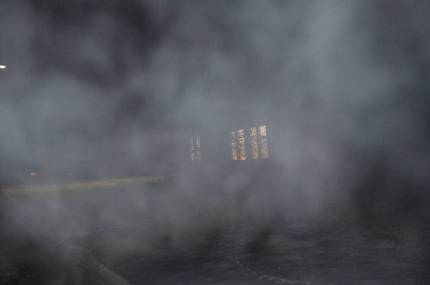 Χιόνι ομίχλη μέσα από την οποία τα φωτισμένα παράθυρα του σπιτιού είναι αμυδρά ορατά. - Φωτογραφία, εικόνα