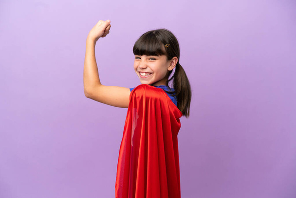 Klein kind geïsoleerd op paarse achtergrond in superheld kostuum en het doen van sterke gebaar - Foto, afbeelding