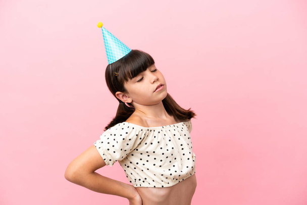 Pequena criança caucasiana com chapéu de aniversário isolado no fundo rosa sofrendo de dor nas costas por ter feito um esforço - Foto, Imagem