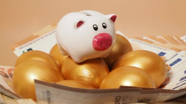 Ovos dourados, dinheiro e porquinho. Ovos de galinha dourados e notas de euro. Símbolo da riqueza. Imagens 4k de alta qualidade - Filmagem, Vídeo