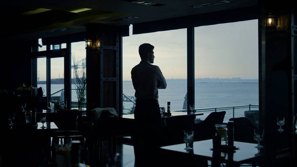 Focused man silhouette looking beautiful view in dark panoramic bar. Handsome boss waiting business meeting in restaurant. Charming businessman enjoying time in lounge cafe. Modern lifestyle concept. - Foto, imagen
