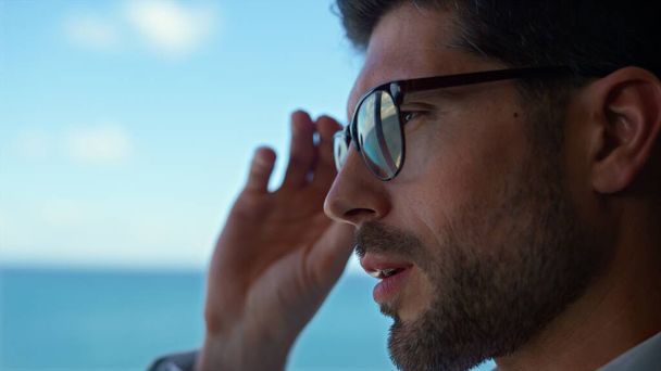 Frustrated man taking off glasses at sea view closeup. Tired ceo leader feeling exhausted in panoramic window office. Bearded businessman haggard after work trying relax at overlooking ocean hotel - Foto, afbeelding