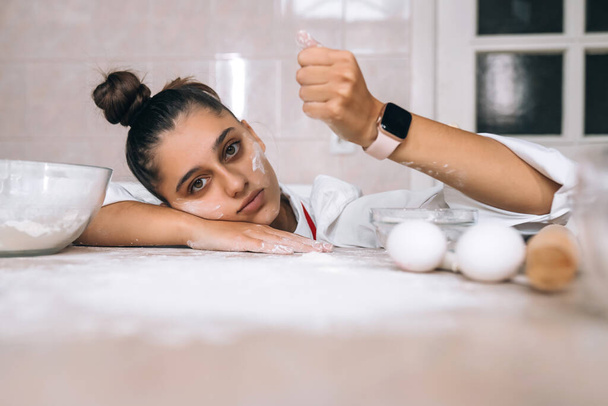 Zmęczona młoda kobieta wylewa mąkę na stół kuchenny, widok z bliska - Zdjęcie, obraz