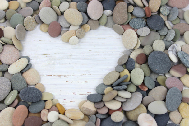 Çakıl taşları üzerinde beyaz bir sıkıntılı ahşap backgro ile yapılan kalp şekli - Fotoğraf, Görsel
