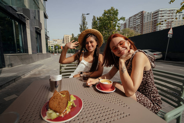 Dos mujeres jóvenes hermosas novias hablando en un café al aire libre, chismorreando, contando noticias juntas. Amistad femenina - Foto, imagen