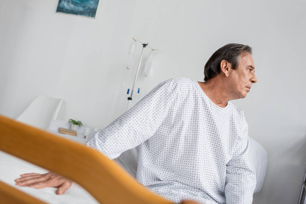 Боковой вид седовласого пациента, сидящего на кровати в клинике - Фото, изображение