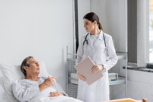 Sick elderly patient talking to doctor with paper folder in hospital - Foto, Imagen