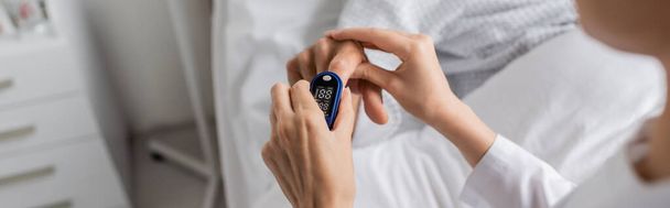 Cropped view of blurred doctor wearing pulse oximeter on finger of senior patient in hospital, banner  - Foto, Imagen