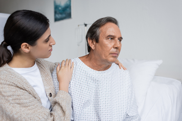 Woman hugging upset dad in patient gown in clinic  - Foto, imagen