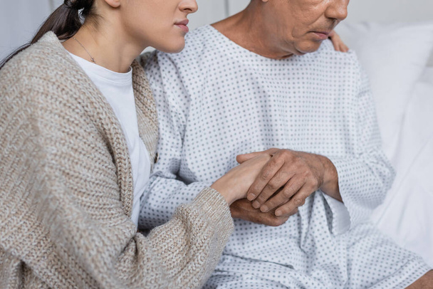 Обрізаний погляд на жінку, що заспокоює старшого батька в одязі пацієнта в клініці
  - Фото, зображення