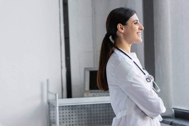 Side view of positive doctor in white coat standing in clinic  - Photo, Image
