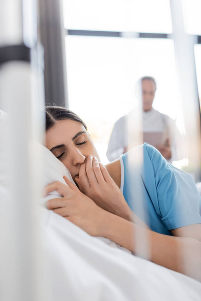 Paciente triste deitado com os olhos fechados na cama na enfermaria do hospital  - Foto, Imagem