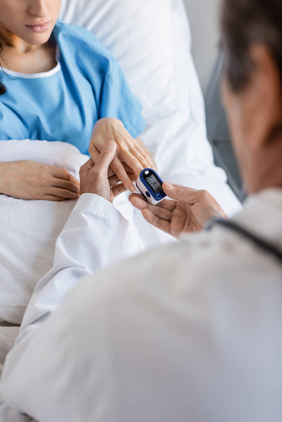 病院で患者の指にパルス酸素濃度計を身に着けているぼやけた医師  - 写真・画像