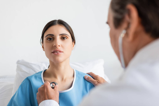 В клинике размытый врач держит стетоскоп возле груди пациента  - Фото, изображение