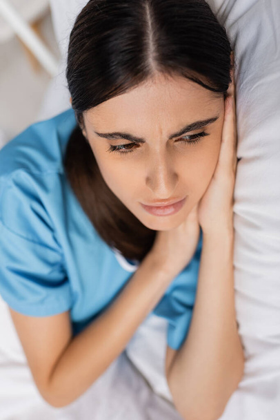 Хвора і засмучена жінка в сукні пацієнта лежить на ліжку в клініці
  - Фото, зображення