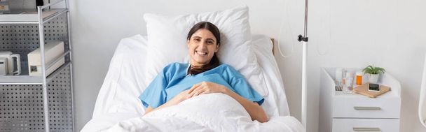 Позитивный пациент улыбается перед камерой на кровати в палате больницы, баннер  - Фото, изображение