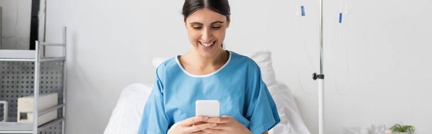 Paziente allegro utilizzando smartphone sul letto in clinica, banner  - Foto, immagini