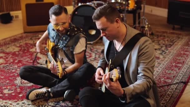 Männliche Gitarristen einer Musikband lernen einen neuen Song, sitzen mit Noten auf dem Boden. Hochwertiges 4k Filmmaterial - Filmmaterial, Video