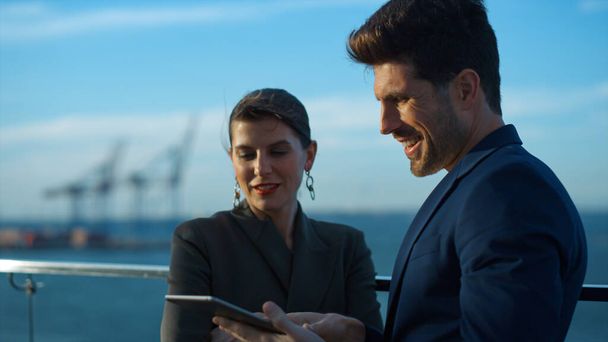 Work couple using tablet outdoors sunlight closeup. Business partners discussing financial results check online data at sea view. Smiling colleagues talk on office balcony. Professionals team concept - 写真・画像