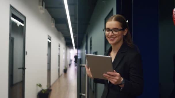 タブレットウォーキングオフィスホールに触れる笑顔ビジネス女性。成功した結果をオンラインで点検するコンピュータを使用して幸せなCEOの専門家。魅力的なフリーランスの若い弁護士が廊下に行く電子メールを送る. - 映像、動画
