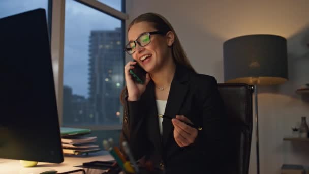 金融管理者が遅くまでオフィスにいる携帯電話を話してる。笑顔の女性は夜にビジネスパートナーとマーケティングプロジェクトを議論仕事。暗い職場で働きすぎるフレンドリーなジャーナリストCEO. - 映像、動画