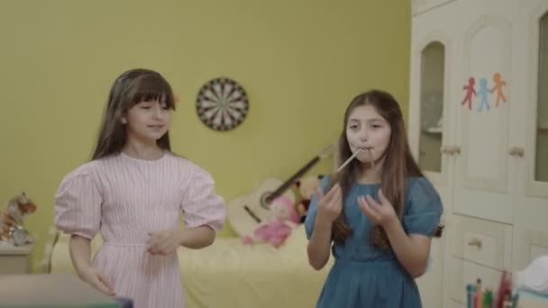 Little girls are having fun together by dancing in their room at home. Happy girls are having a crazy party at their house. Funny kids dancing, jumping, singing are sending air kisses to the camera. - Filmmaterial, Video