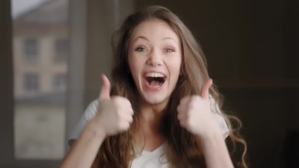 Щаслива захоплена збуджена здивована кавказька молода жінка, дивлячись на камеру, показуючи великі пальці вгору, радіючи досягненню відмінного результату, демонструє узгодження жестів знак з радістю
 - Кадри, відео