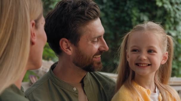 Close up Caucasian adult parents bearded father dad and mother talking funny smile laugh speak happy conversation with small cute child girl daughter daddy cuddle hug baby laughing together outdoors - Footage, Video
