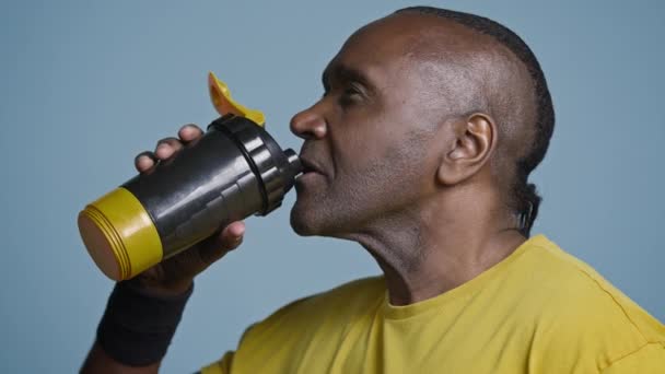 Zbliżenie zmęczony sportowiec robi sobie przerwę podczas treningu picie zimnej wody słodkiej z butelek sportowych gasi pragnienie po wysiłku dorosły afrykański sportowiec cieszący się napojem proteinowym - Materiał filmowy, wideo