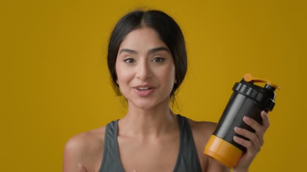 Web kamera görüntüsünü kapatın. Stüdyo sarı arka planda sporcu bayan sporcu bayan sporcu bayan talk show fitness şişesiyle su likörü protein kokteyli karıştırıcı ile konuşuyor. - Video, Çekim