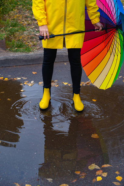 um guarda-chuva multicolorido e botas amarelas em uma poça. Foto de alta qualidade - Foto, Imagem