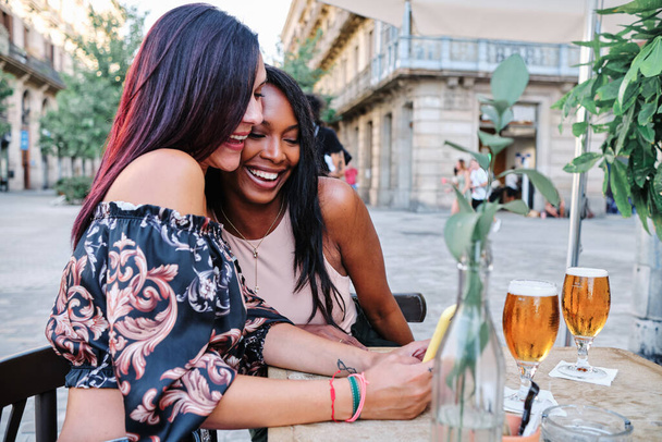 Perfil de dois amigos multiétnicos felizes usando um celular no terraço de um bar - Foto, Imagem