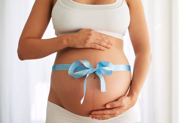 Це не великий подарунок. жінка з блакитною стрічкою, пов'язаною навколо її вагітного живота
 - Фото, зображення