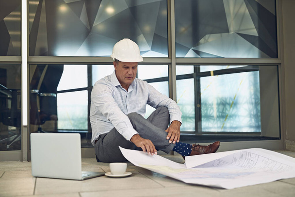 Он тоже работает над перерывами. сфокусированный профессиональный мужчина-архитектор, сидящий на полу во время работы над ноутбуком - Фото, изображение