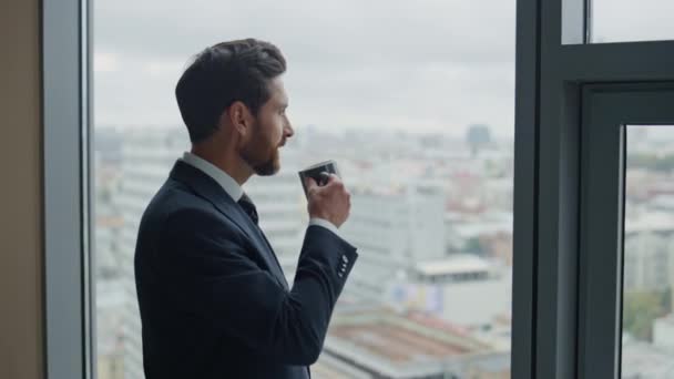 Kendine güvenen sakallı CEO yönetici ofis penceresinde dikilirken kahve molasının tadını çıkarıyor. Rahatlamış iş adamı şehir manzaralı bir içecek içiyor. Girişimci yönetici iş fırsatları üzerine düşünüyor - Video, Çekim