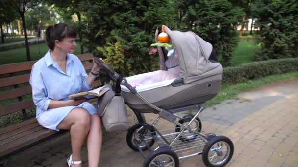 Mama mit Kinderwagen atmet frische Luft im Park. Eine Frau liest ein Buch. 4K Slow Mo - Filmmaterial, Video
