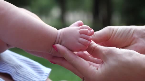 Close-up vrouwelijke handen strelen babys voeten. Moeder en kind meisje hechting en plezier buiten in de natuur. 4K Slow Mo - Video