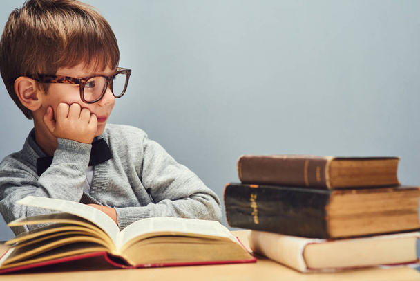 Aprendes algo nuevo todos los días. Estudio de un niño inteligente leyendo libros y mirando pensativo sobre un fondo gris - Foto, imagen
