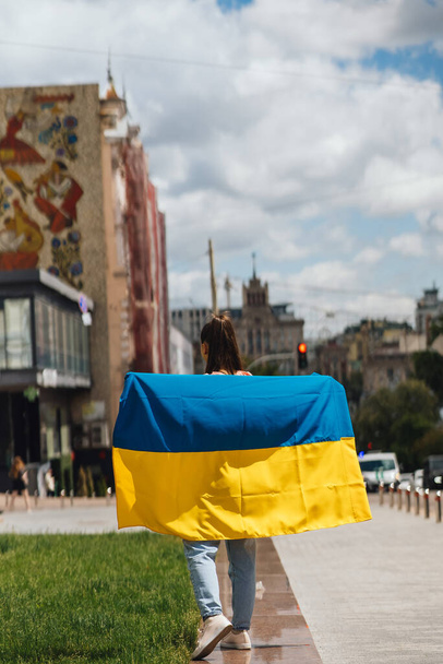 Mujer joven con bandera nacional de Ucrania caminando por la ciudad - Foto, imagen
