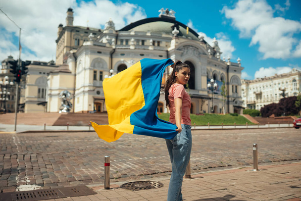 Νεαρή γυναίκα με εθνική σημαία της Ουκρανίας περπάτημα στην πόλη - Φωτογραφία, εικόνα