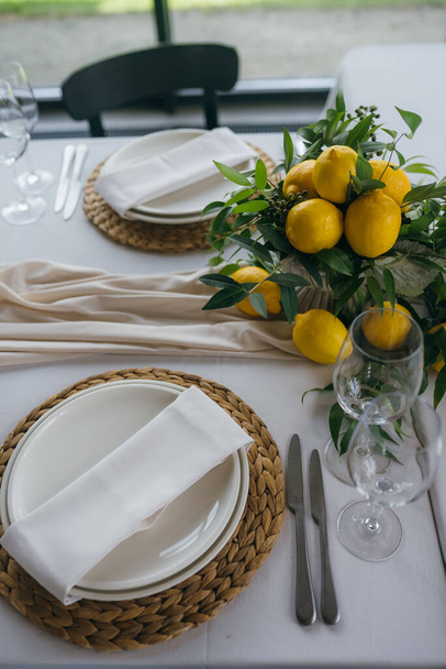 Slavnostní stůl na svatebním večírku zdobí citrónové aranžmá, na stole jsou talíře s ubrousky a sklenicemi - Fotografie, Obrázek