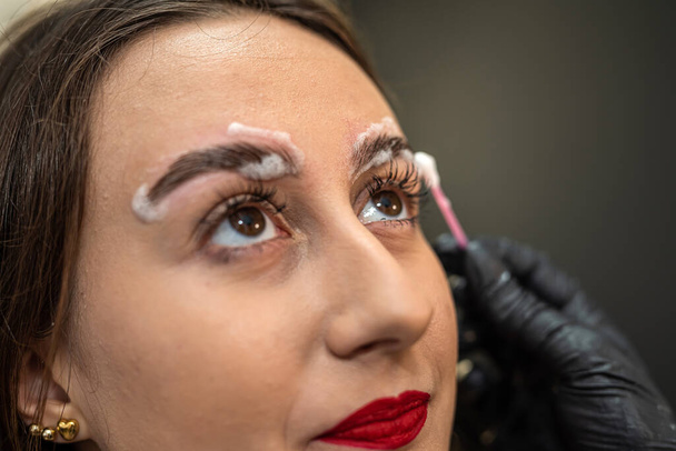 Wimpernmacher trug Augenbrauen-Kaschierschaum auf die Augenbrauen des Kunden auf. Augenbrauen-Konzept. Lackierung und Laminierung - Foto, Bild